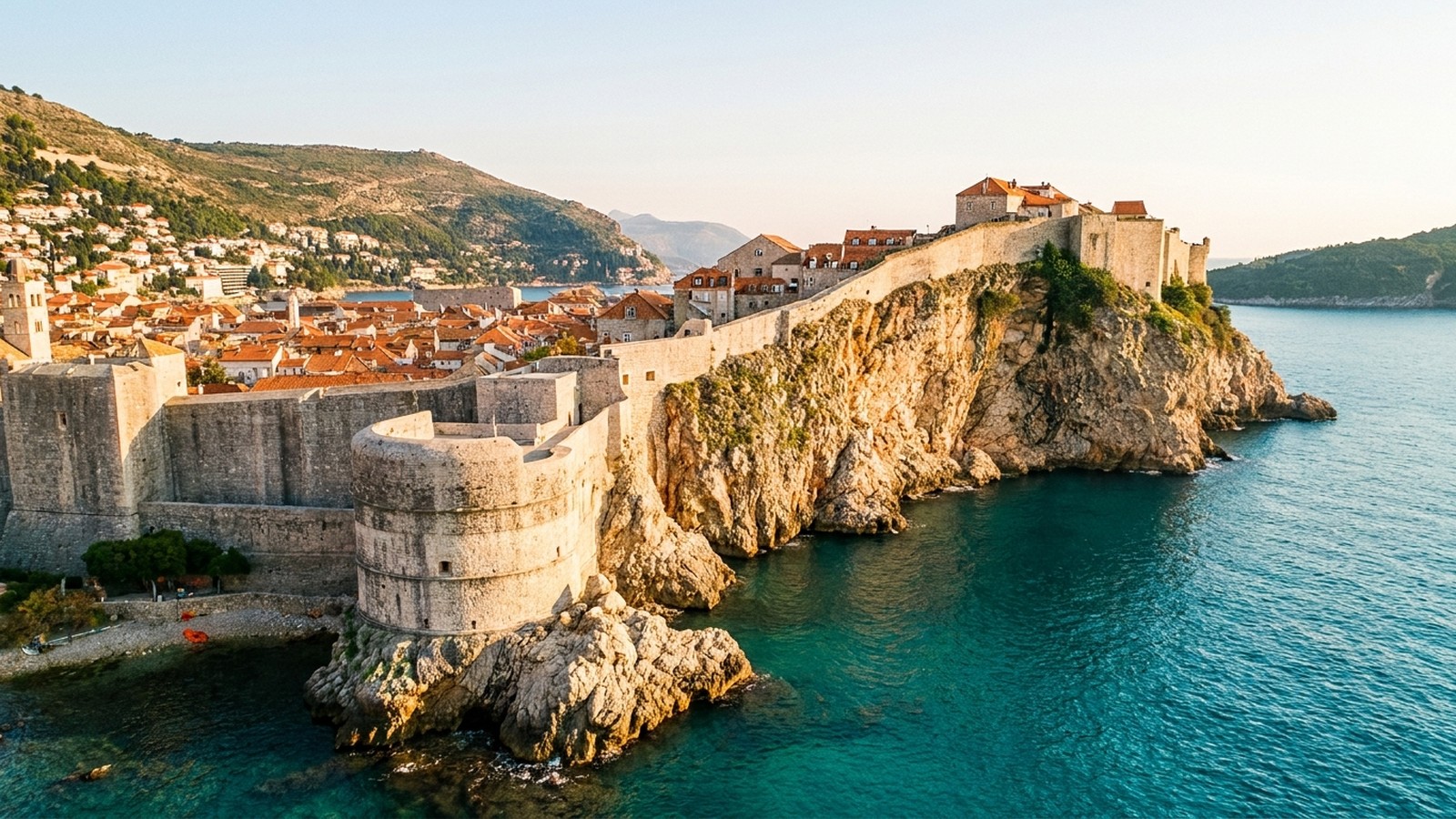 Cité médiévale fortifiée aux remparts de pierre dominant une mer turquoise au coucher du soleil