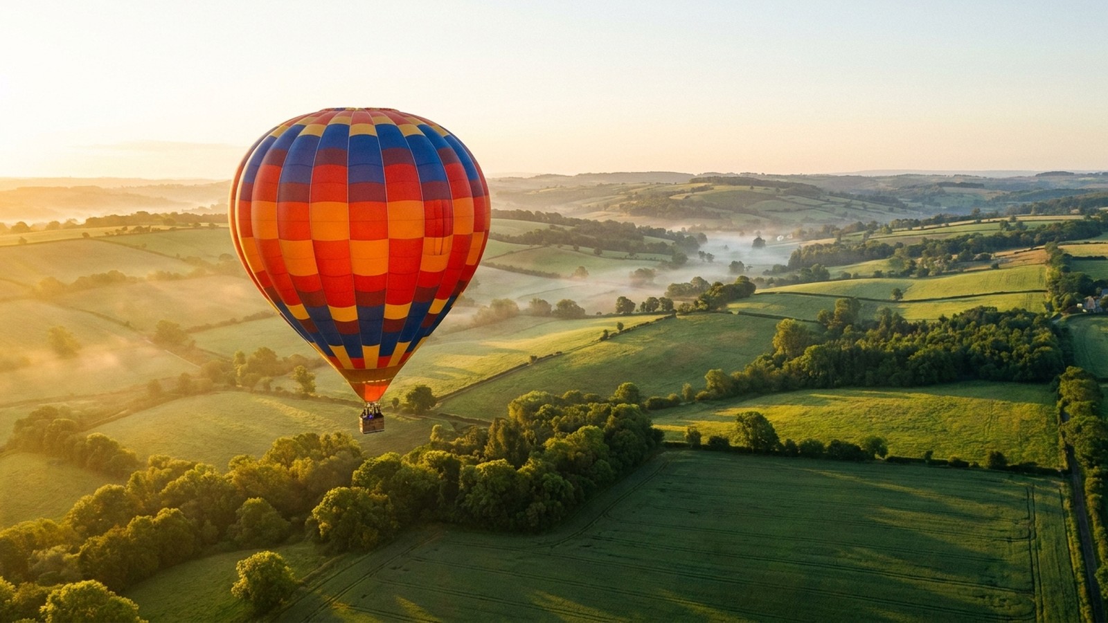 Une montgolfière colorée s'élevant dans un ciel clair au lever du soleil au-dessus d'une campagne verdoyante, ambiance paisible