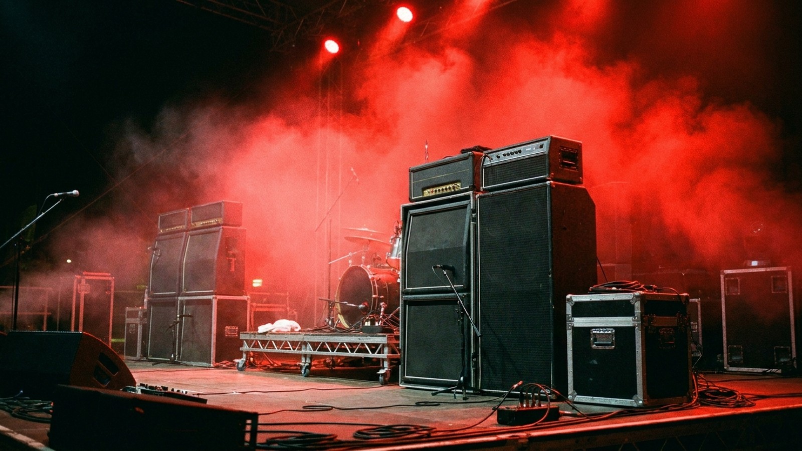 Une scène de concert rock la nuit avec des amplis noirs et des projecteurs rouges